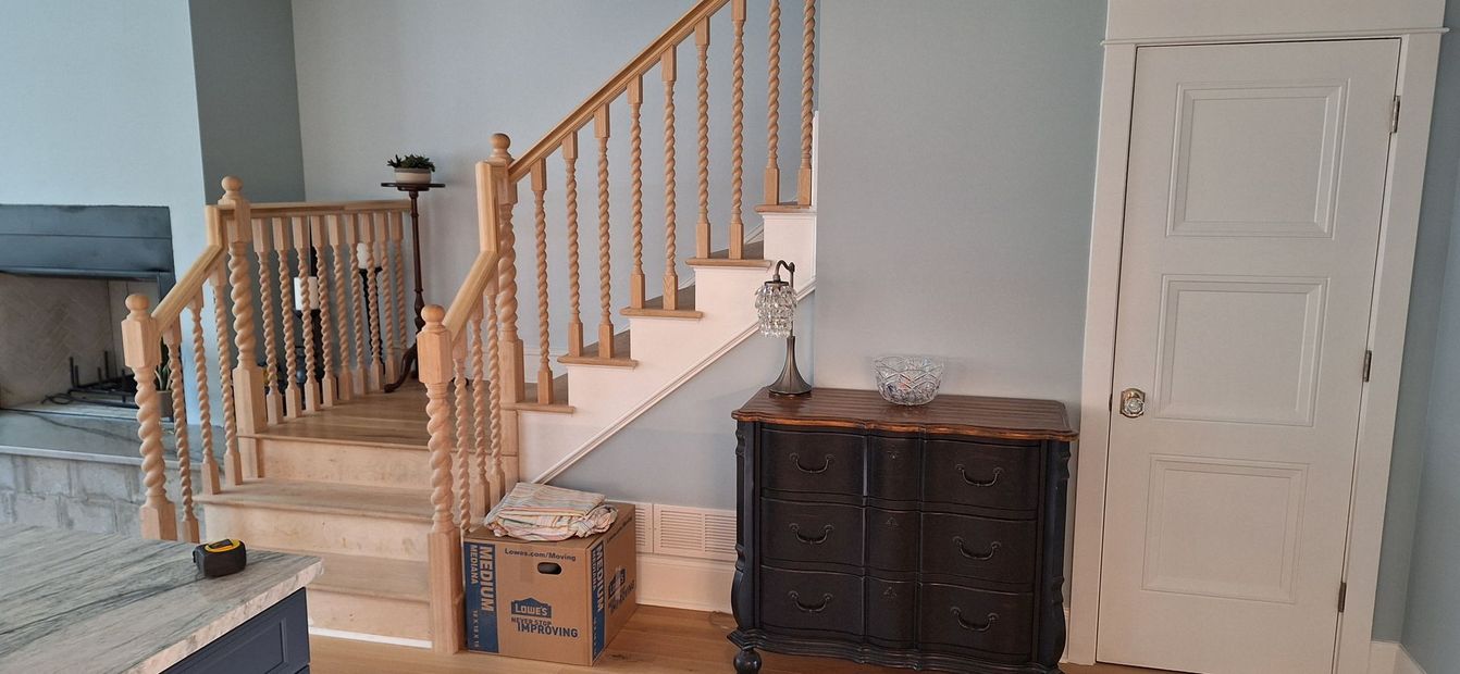 A living room with stairs , a dresser , and a door.