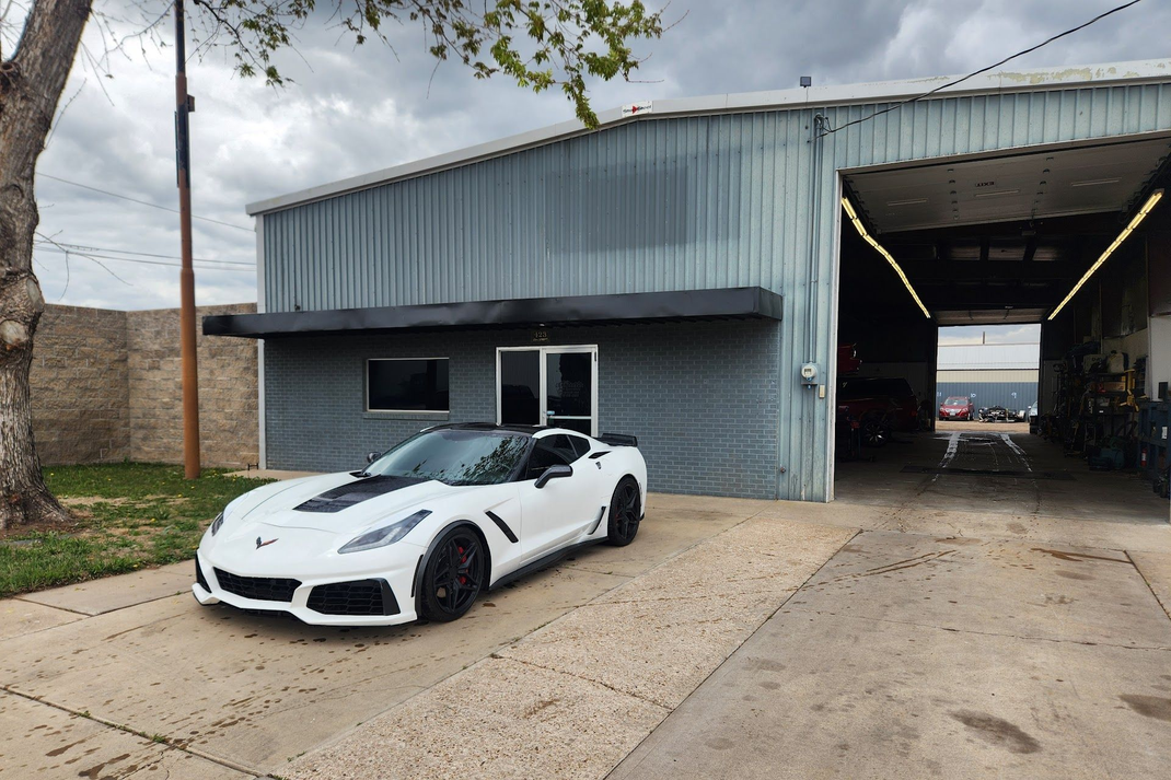 White sports car parked in front of a gray metal building with an open garage bay. | CRF Automotive Specialists