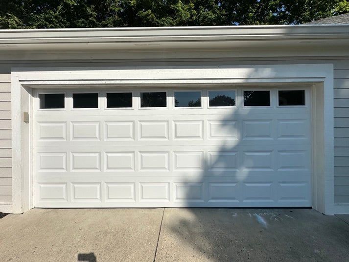 White garage door with windows, set in a white frame. Sunlight casts a shadow across it.