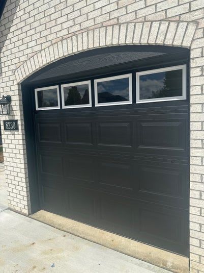 Black garage door with four window panes, set in brick archway.