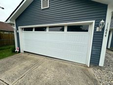 White garage door on a gray concrete driveway, with blue house siding and address number.