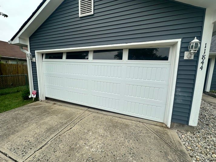 White garage door on a blue house, with a concrete driveway. House number 