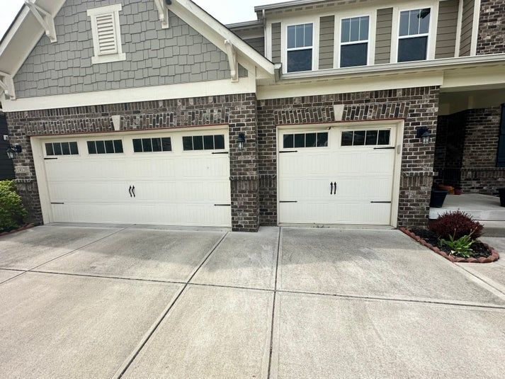 Two white garage doors on a house with brick and gray siding. Concrete driveway in front.