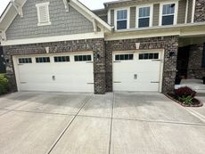 Two white garage doors on a house with brick and gray siding. Concrete driveway in front.