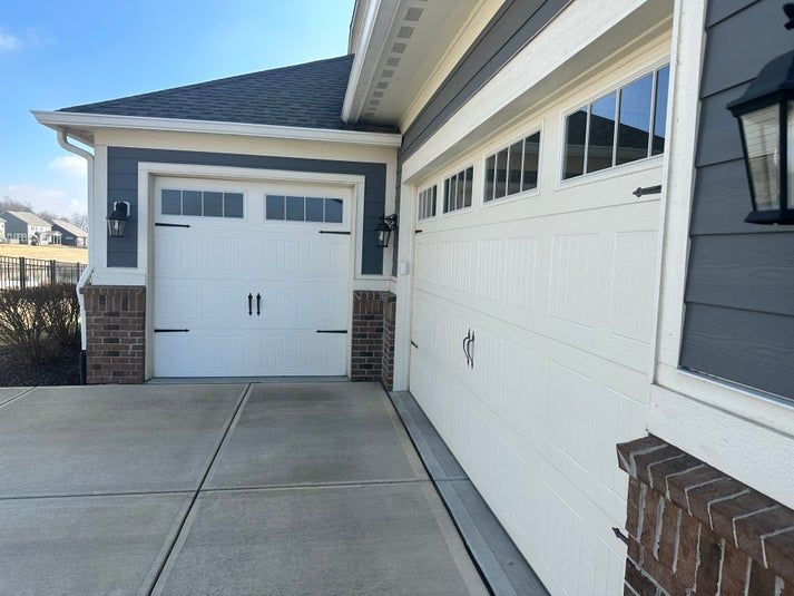 White garage doors on a house with blue siding, brick accents, and concrete driveway.
