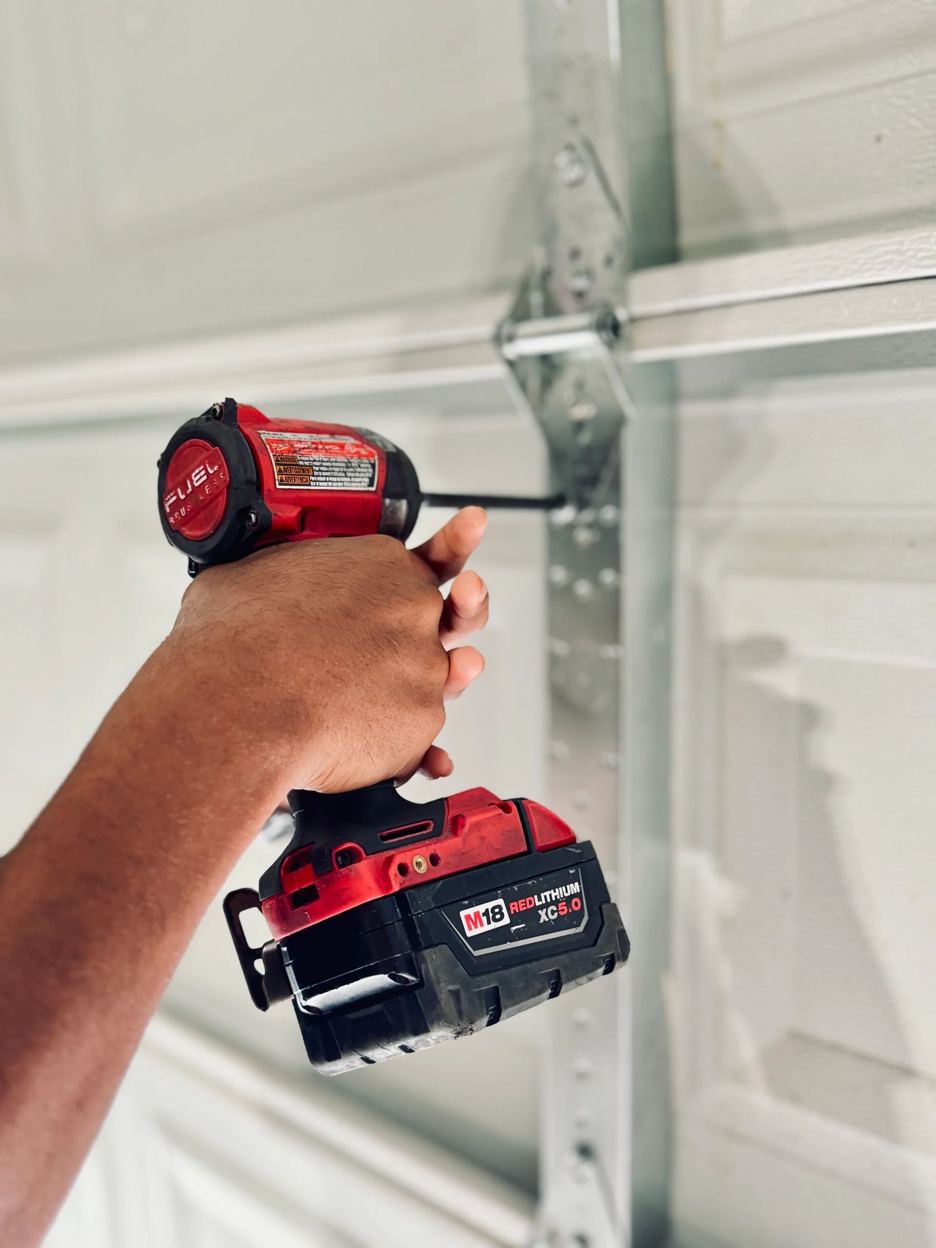 Person using a red power drill to secure a metal bracket on a white garage door.