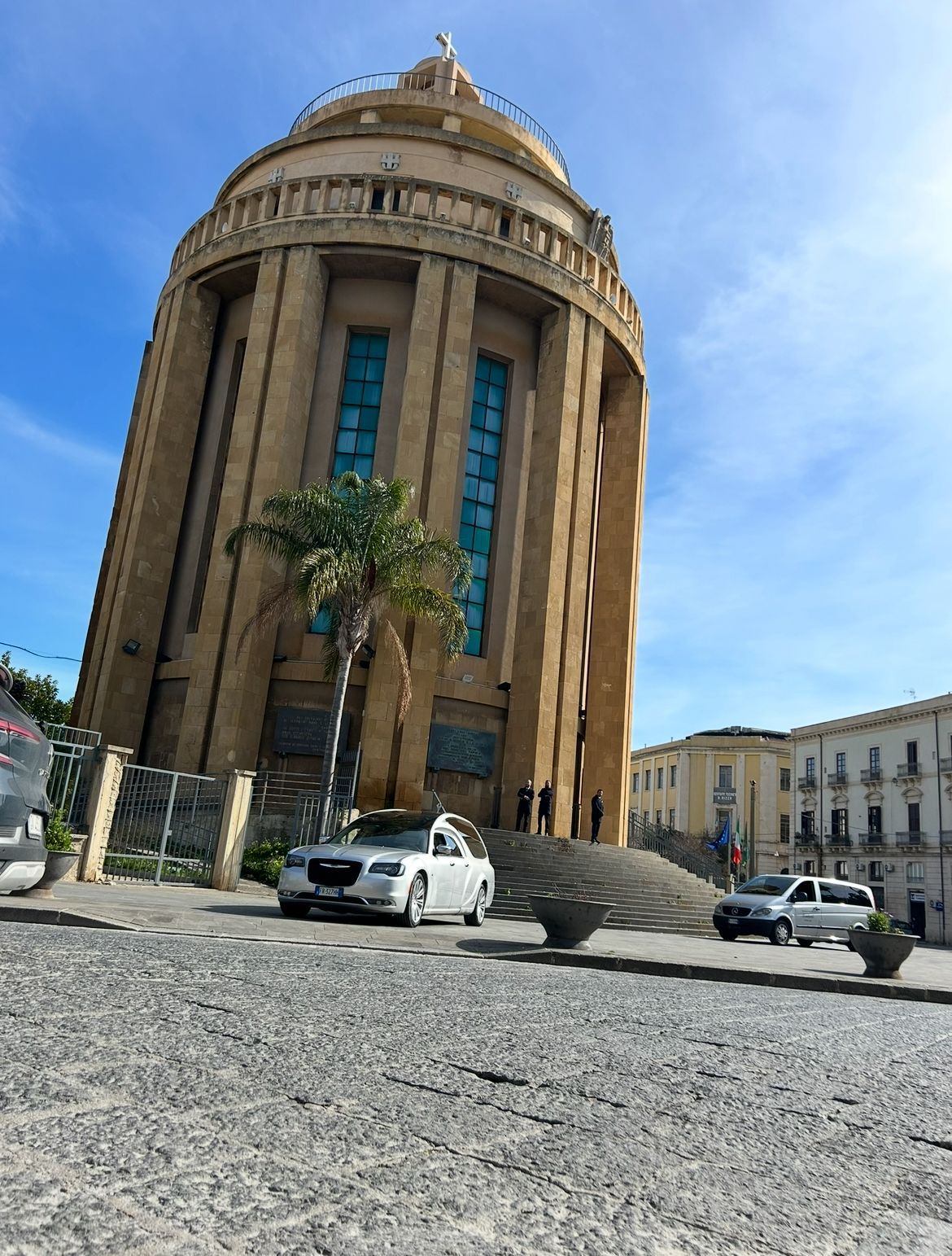 Carro funebre argentato parcheggiato sulla ghiaia in un luogo soleggiato all'aperto.