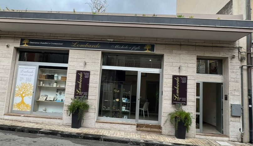 Vetrina con porta e finestre in vetro, piante e insegne in un edificio in mattoni beige.