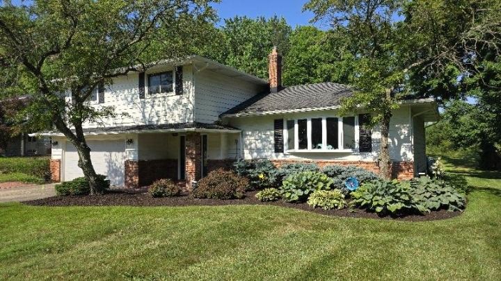 A white house with a large lawn in front of it surrounded by trees.