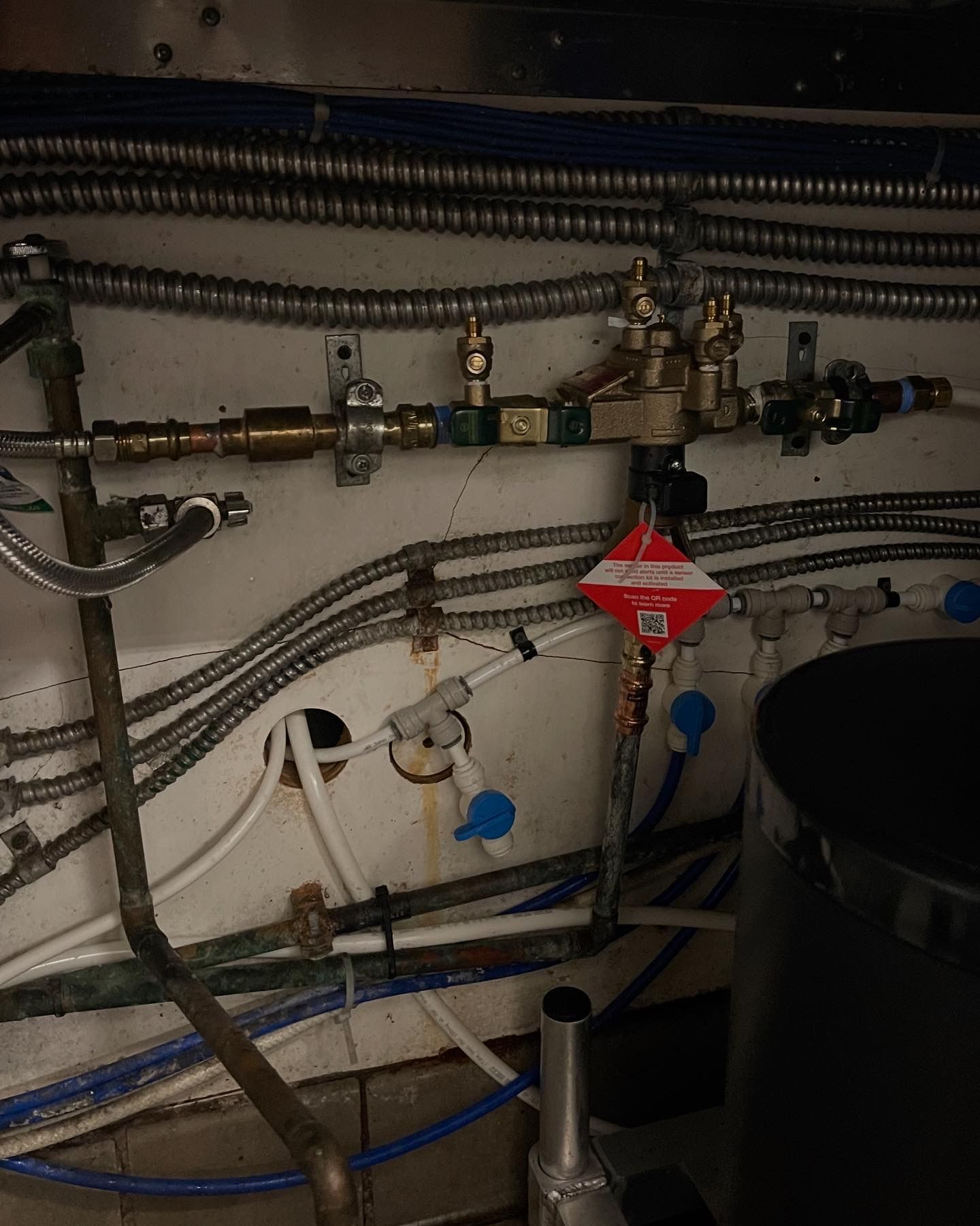 Plumbing pipes and valves on a wall.  Silver corrugated tubing, white and blue pipes, brass fittings.