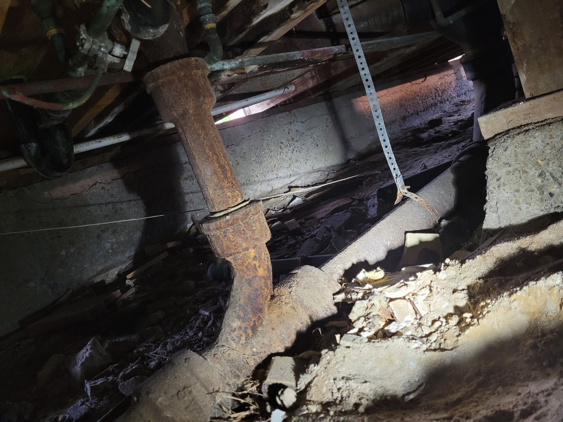 Rusty pipe in a dark crawlspace; water damage present on the surrounding surfaces.