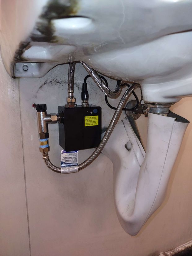 Hands using wrench to tighten a shiny chrome faucet on a white sink.