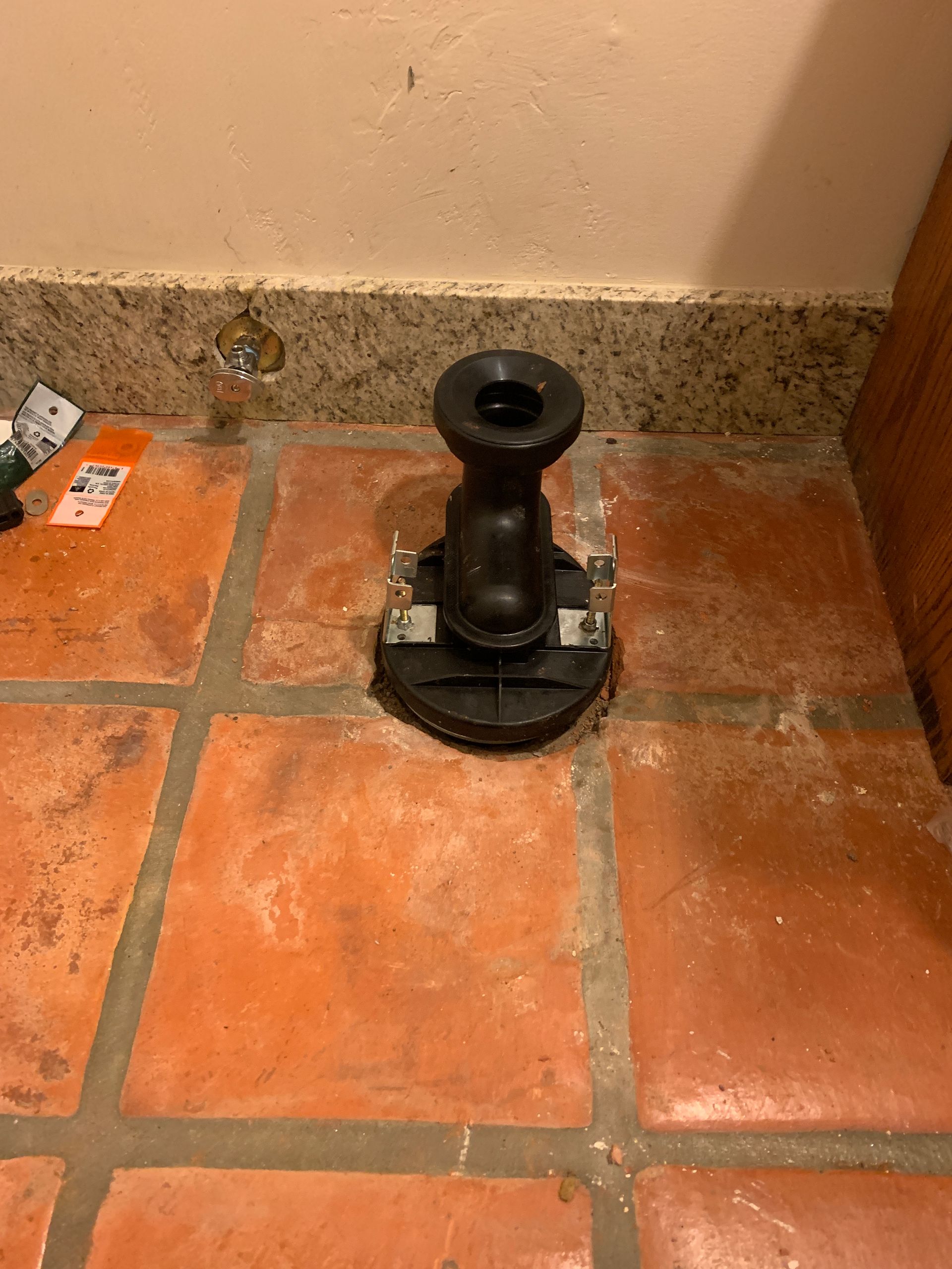 Black plumbing fixture on red tile floor against a beige wall.