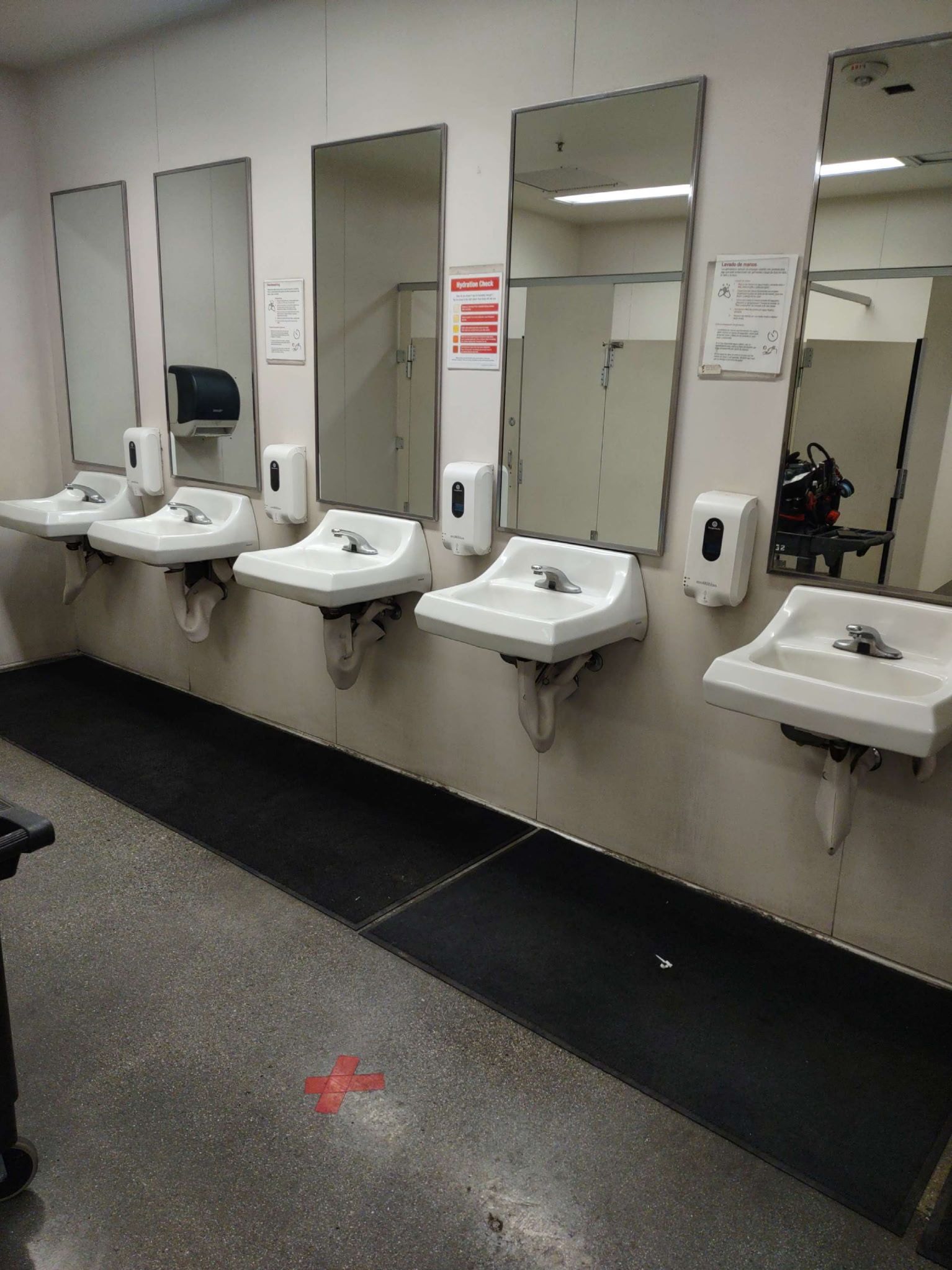 Row of sinks in a public restroom with mirrors, soap dispensers, and a black mat on the floor.