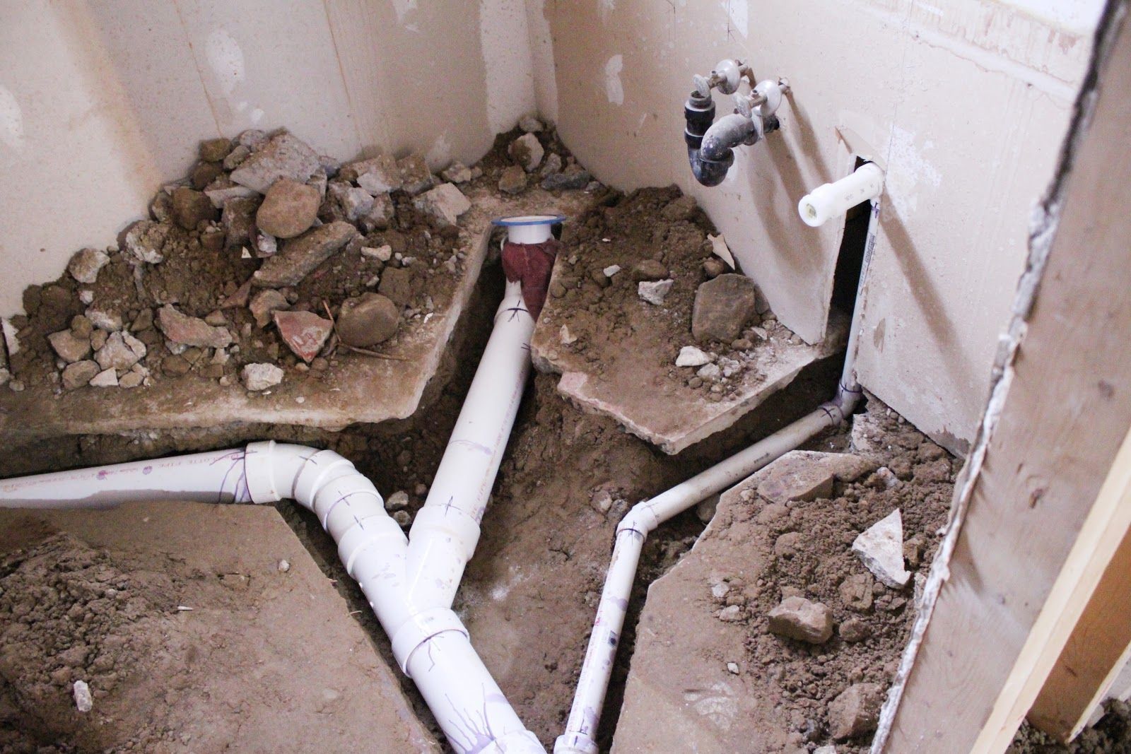 Pipes exposed in dug-up ground, showing plumbing work in a wall.