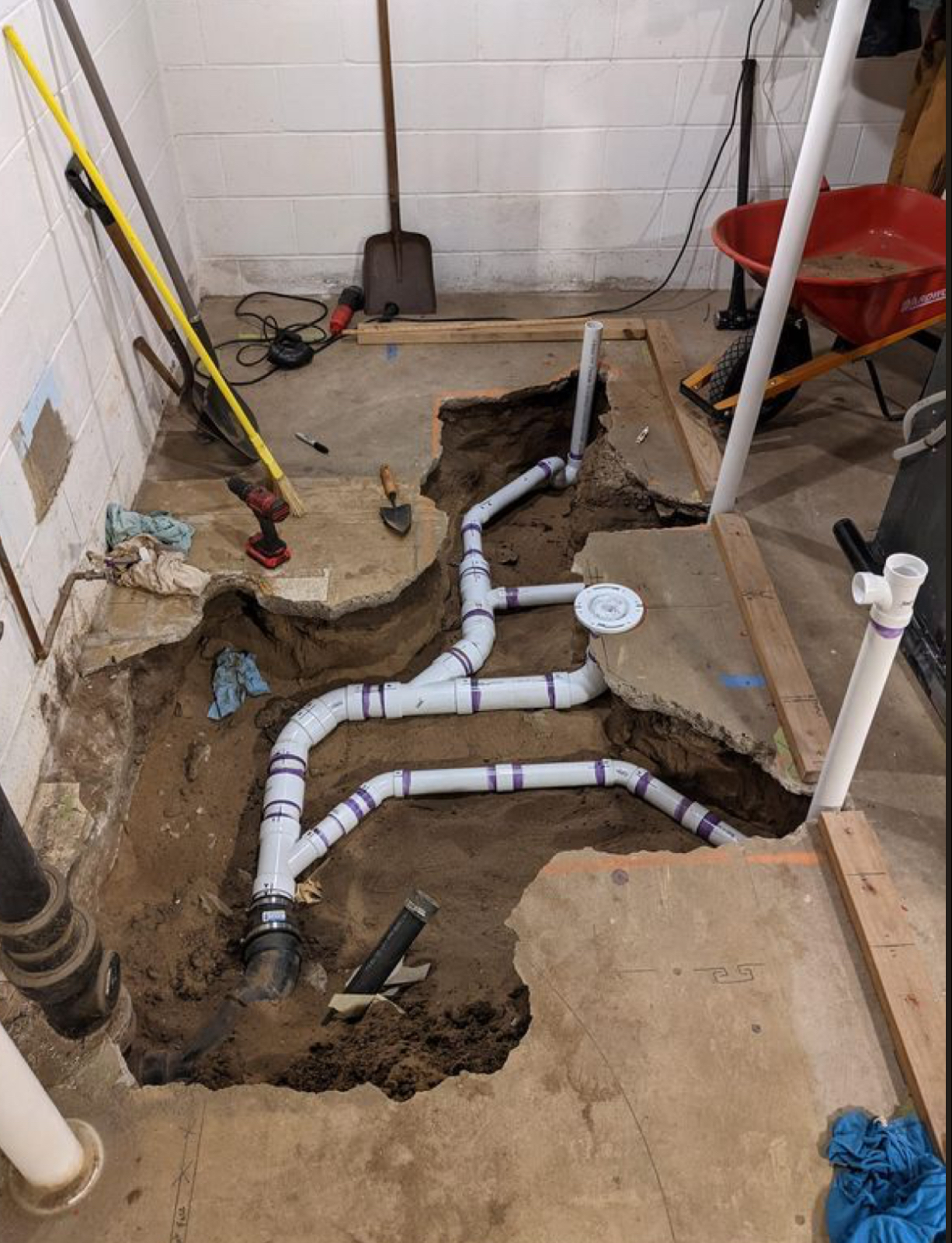 Plumbing pipes exposed in a basement floor excavation for repairs.