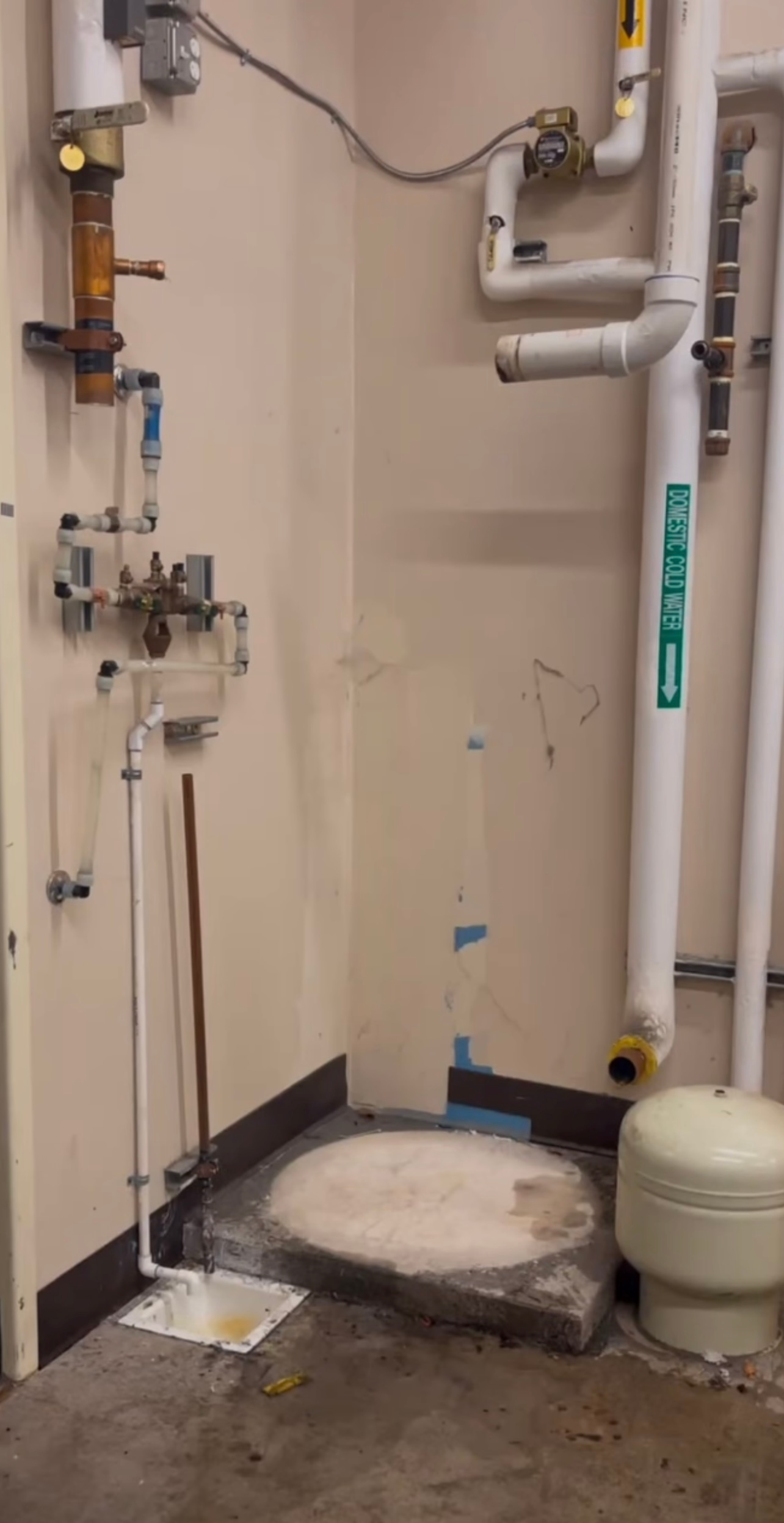 Plumbing in a utility room with pipes, a pressure tank, and floor access.