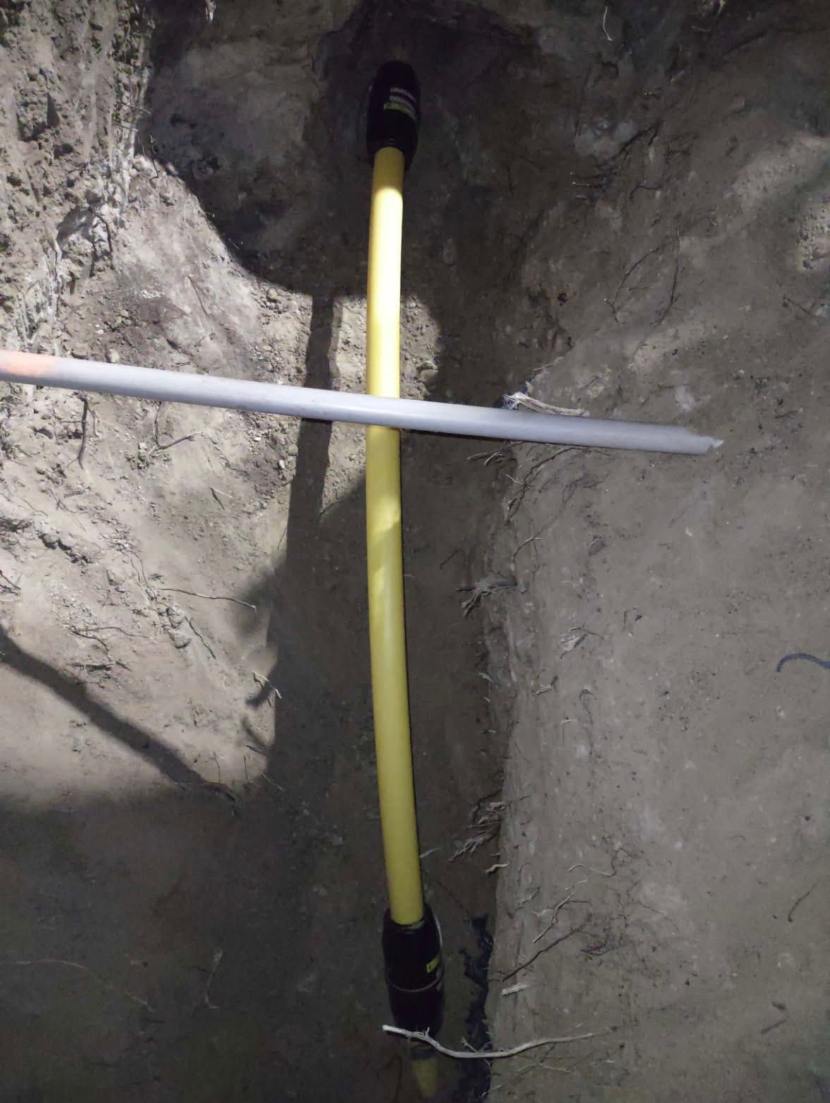 Trench with a yellow pipe running through it, crossed by a horizontal gray pipe.