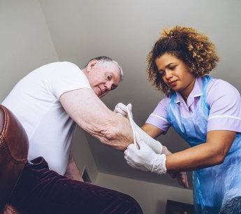 A nurse is putting gloves on an elderly man 's arm.