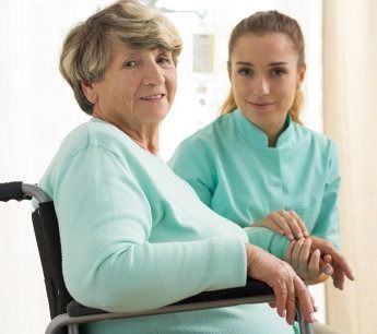 An elderly woman in a wheelchair is sitting next to a nurse.