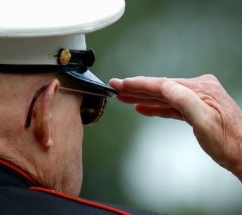 A man in a military uniform salutes with his hand on his hat.