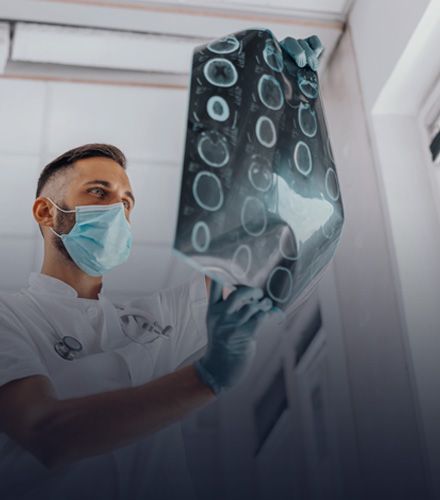 Doctor in mask and gloves examining medical scan in a lit room.