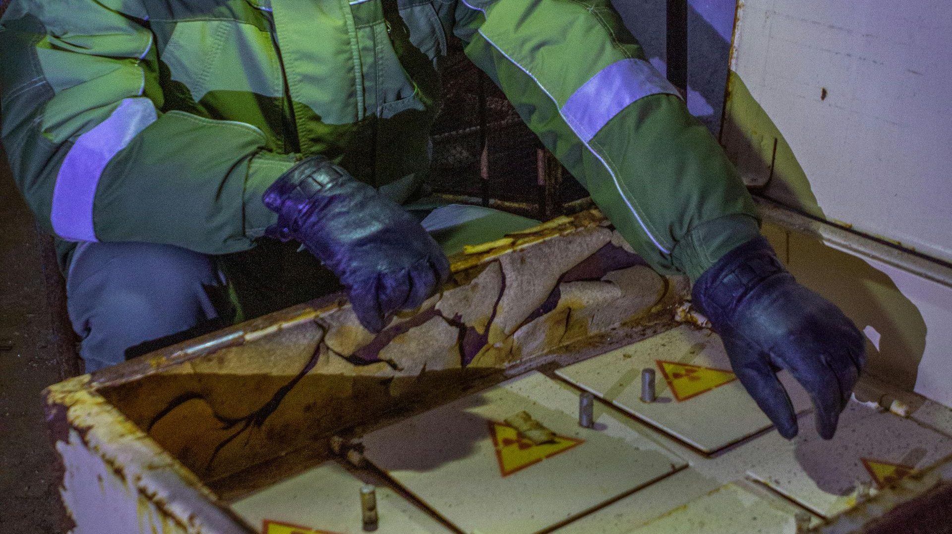 Person in protective suit handling radioactive hazard symbols inside a container.