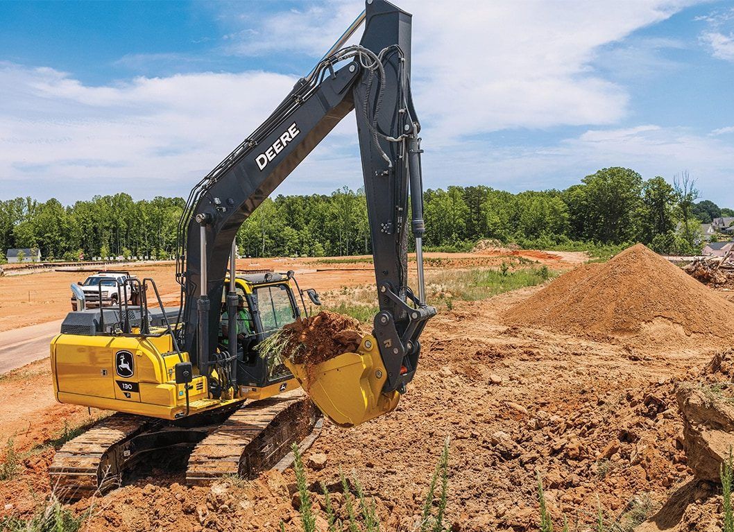 A yellow excavator is digging a hole in a dirt field.
