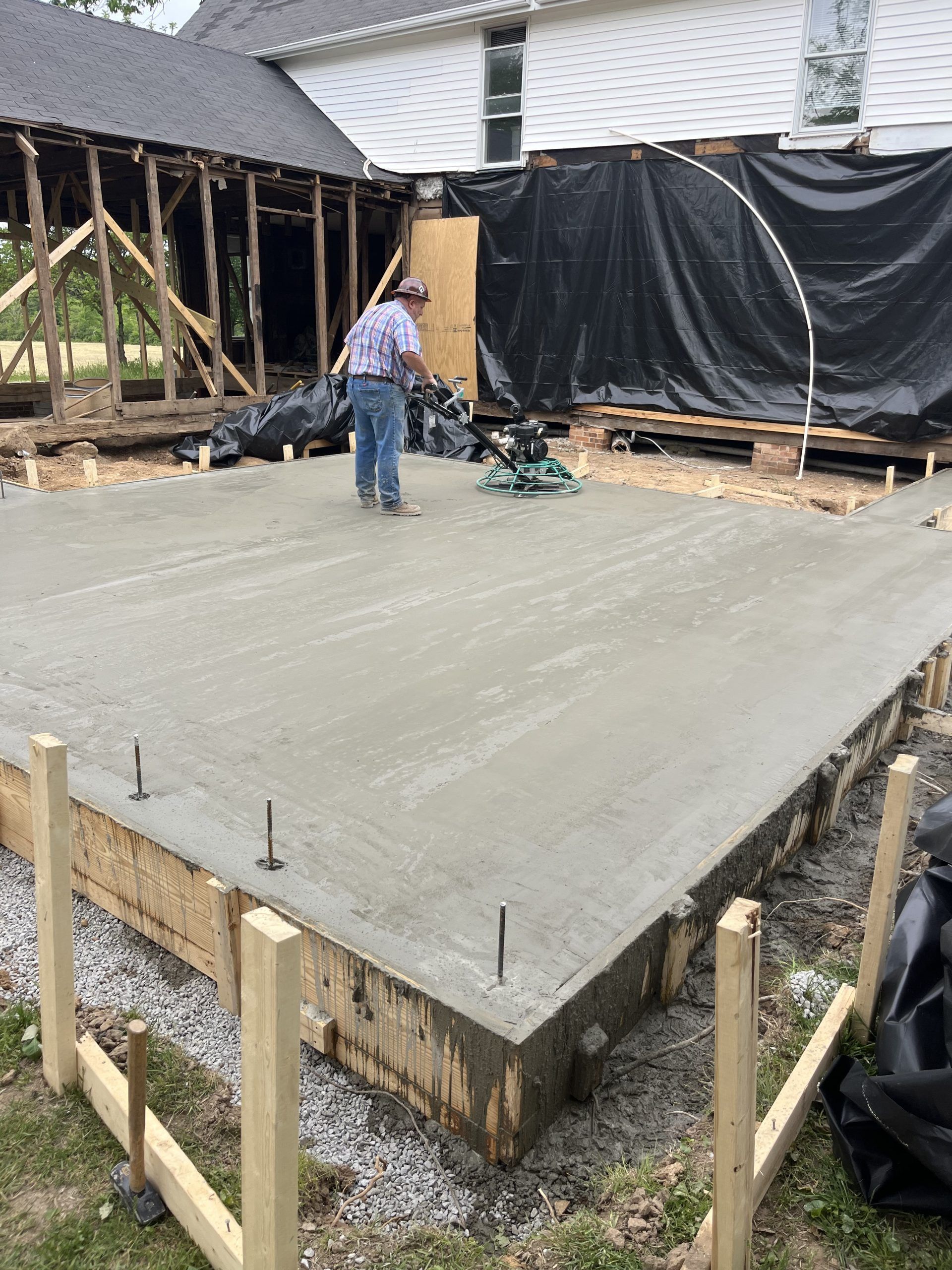 A man is working on a concrete slab in front of a house.