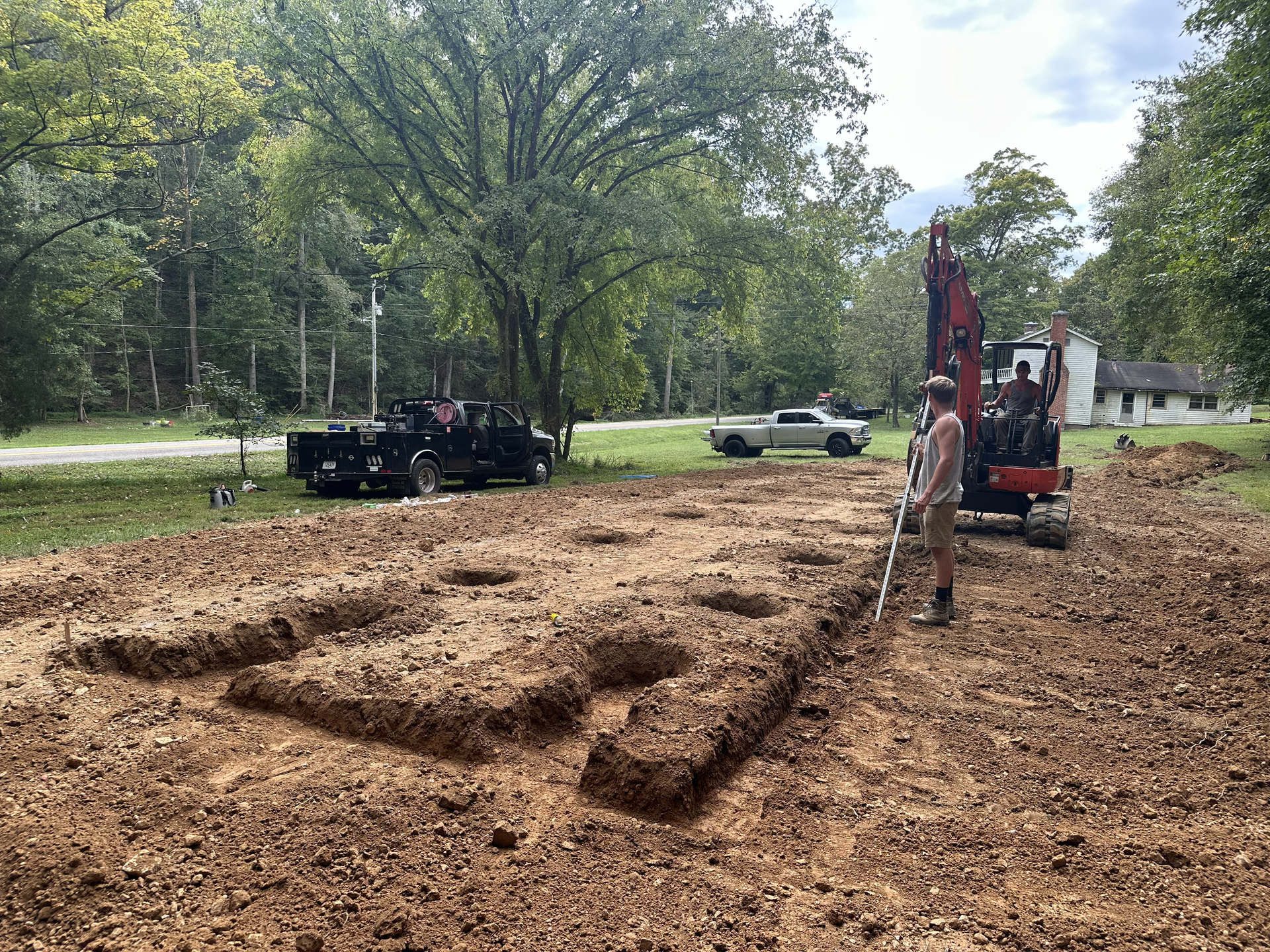 A man is standing in the middle of a dirt field next to an excavator.