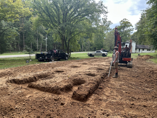 A man is standing in the middle of a dirt field next to an excavator.