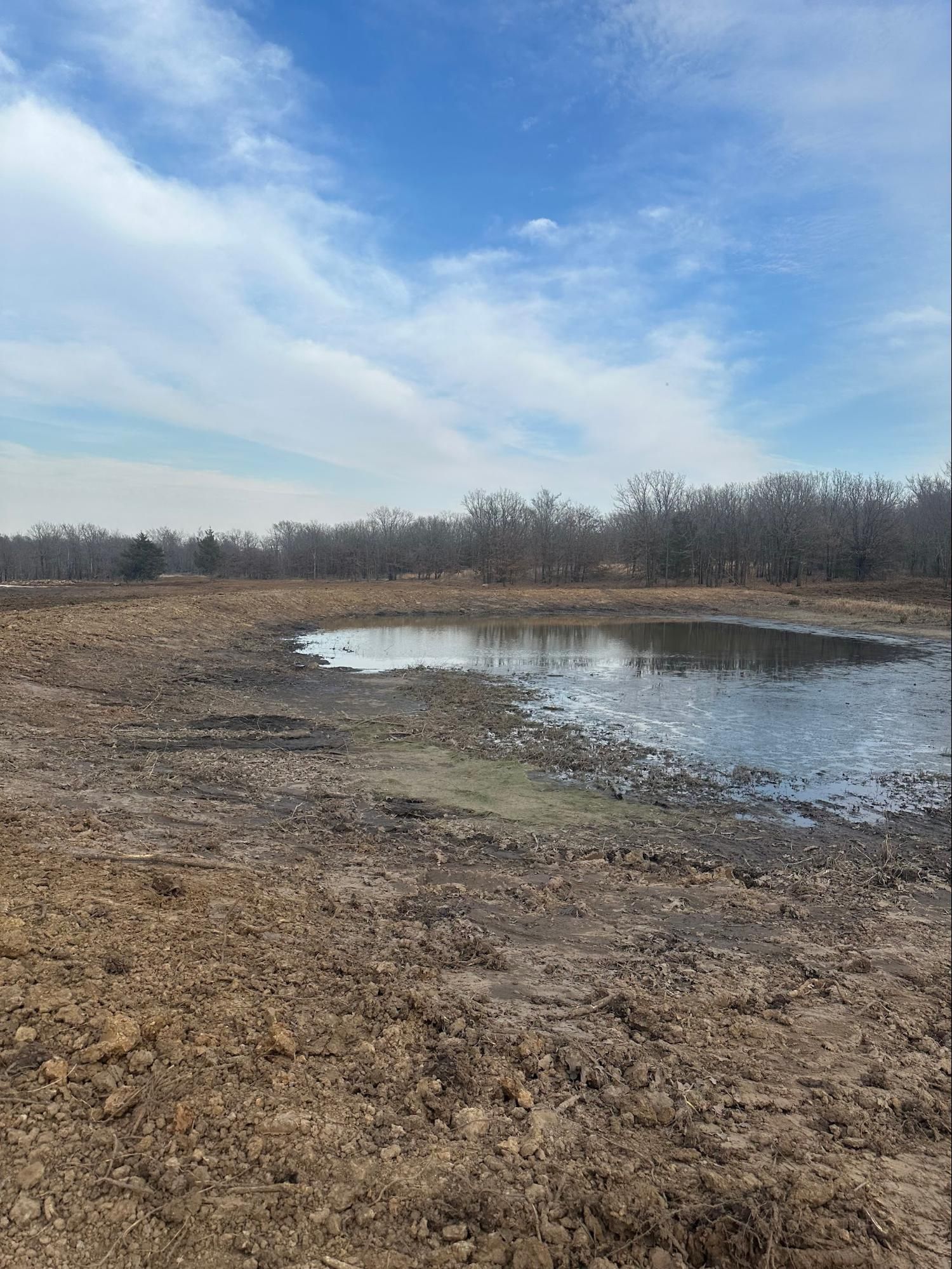 A muddy field with a small pond in the middle of it.
