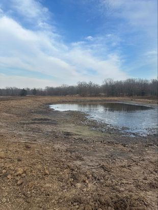 A muddy field with a small pond in the middle of it.