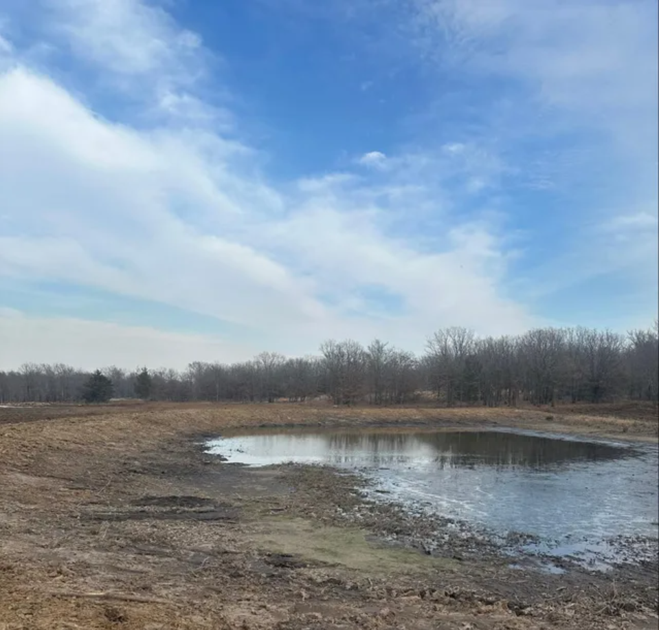 A muddy field with a small pond in the middle of it.
