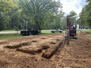 A man is standing in the middle of a dirt field next to an excavator.