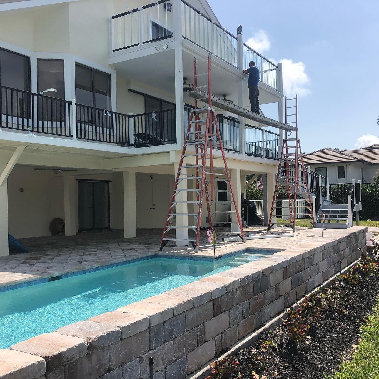 A two-story white house with a pool and a worker on scaffolding.