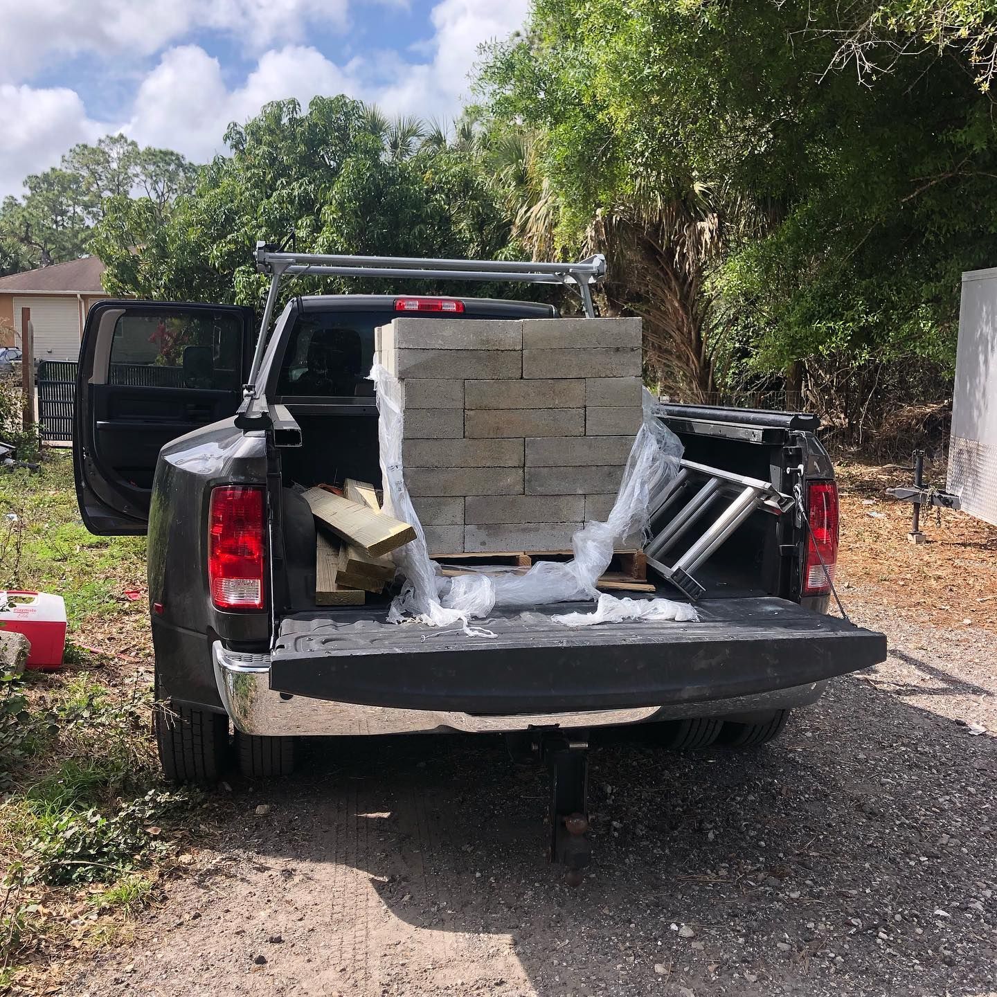 Black pickup truck bed loaded with pavers, lumber, and a ladder, parked outdoors with the tailgate down.