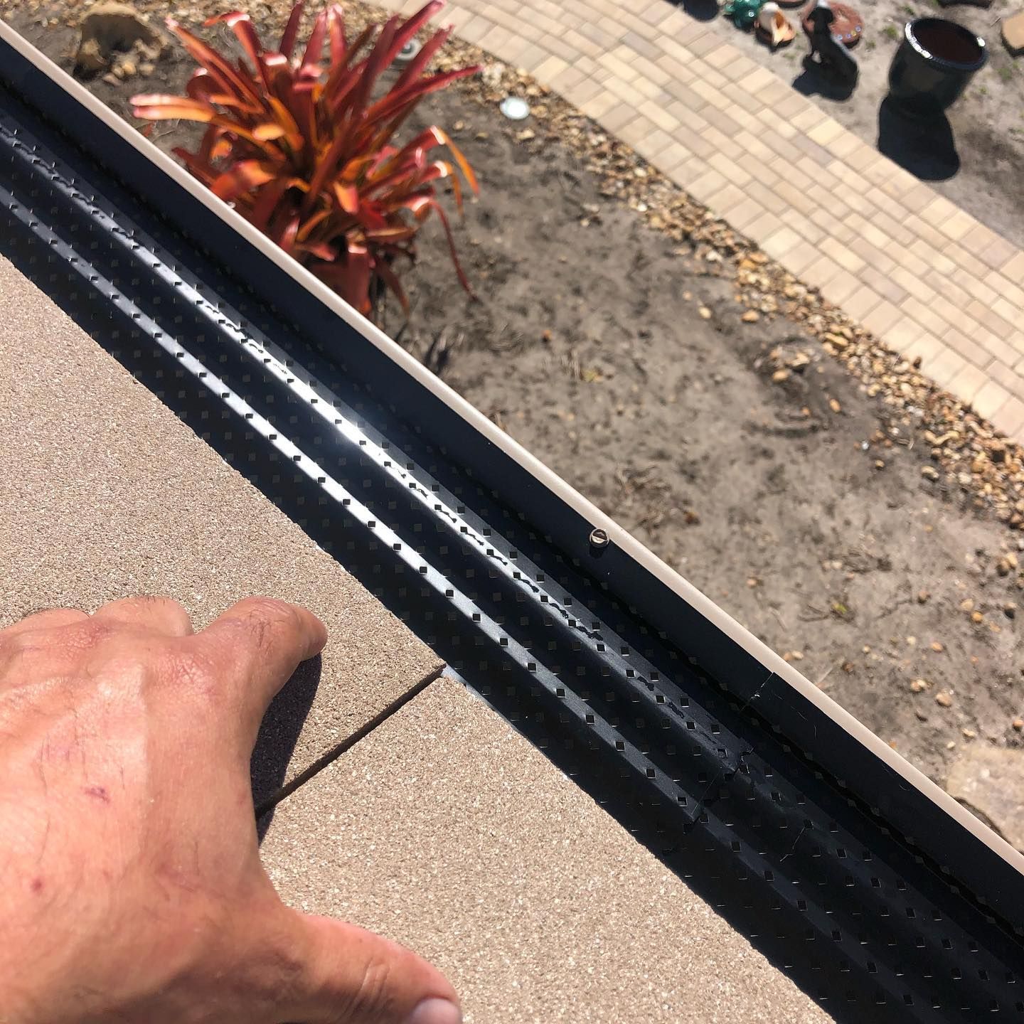 Hand reaching toward a black gutter guard installed on a roof; outdoor setting.