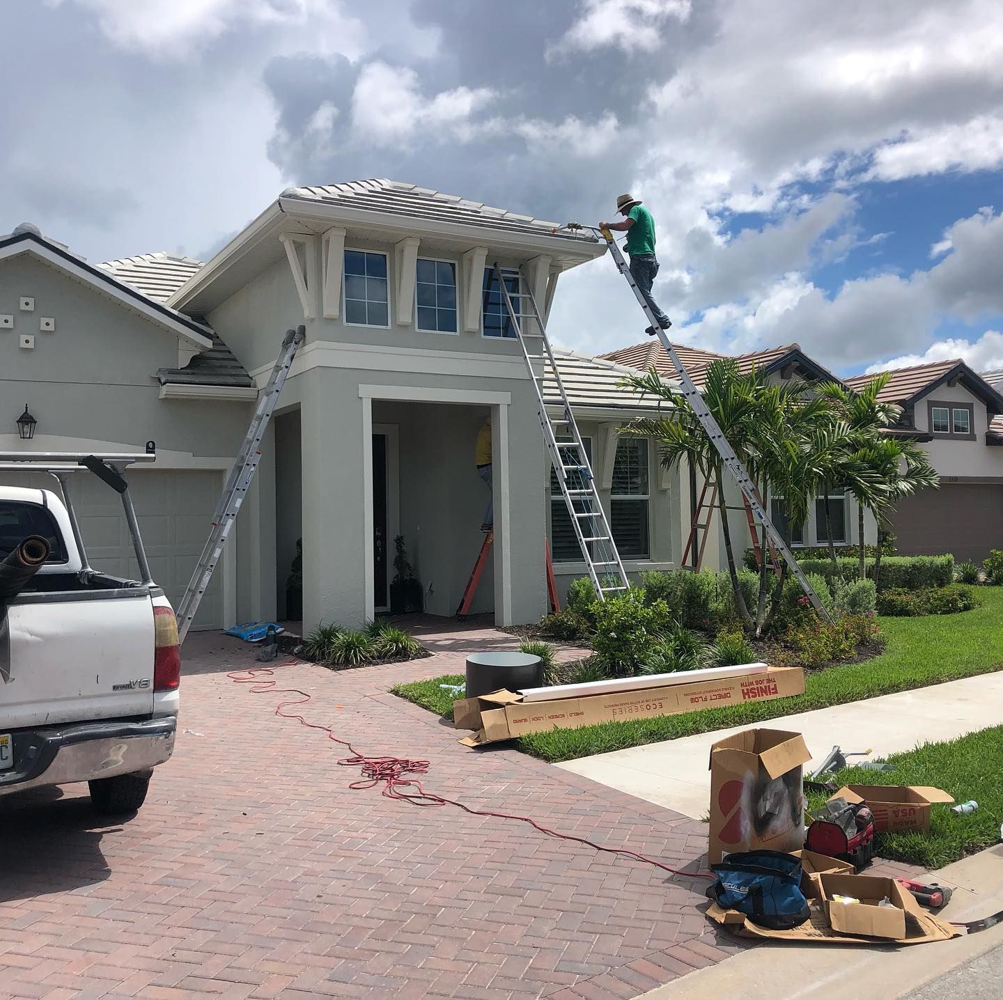 Man on roof, using ladders, working on a house with a gray exterior on a sunny day.