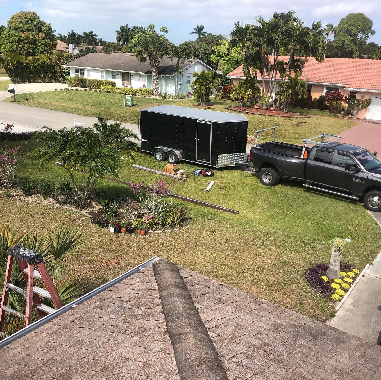 View from rooftop of a residential area with a truck, trailer, and ladder on the lawn.