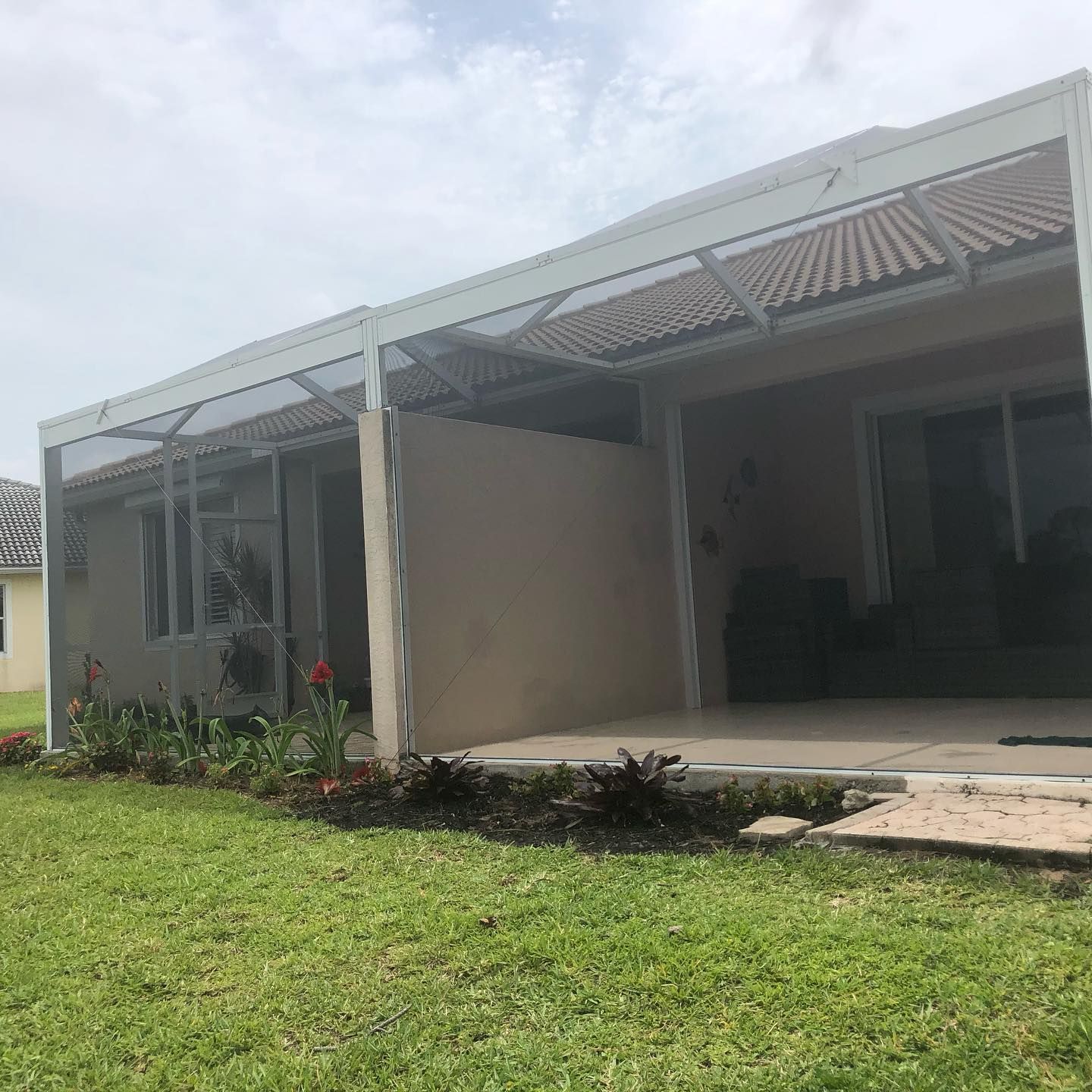 Backyard patio with a screened enclosure and a covered area, green grass, and cloudy sky.