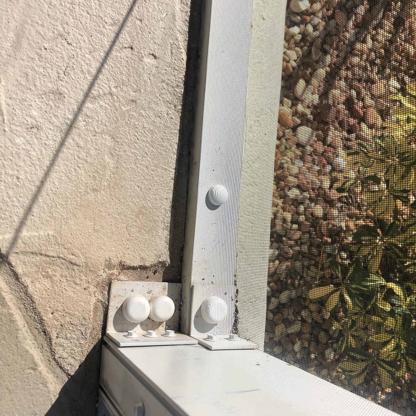 White metal frame bolted to a concrete wall; shadow from sunlight cast on the frame.