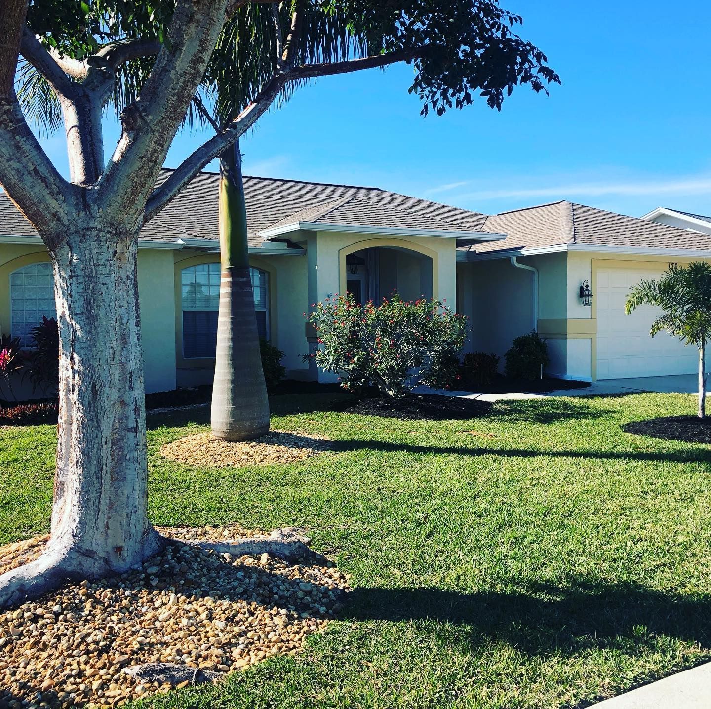 Single-story house with beige walls, a brown roof, and lush green lawn under a clear blue sky.