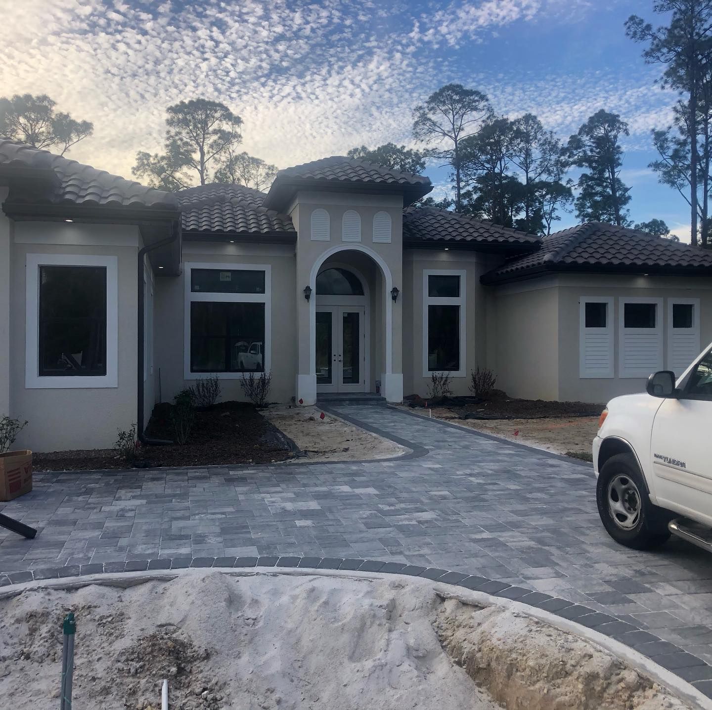 Beige house with gray paver driveway. White truck parked on right.