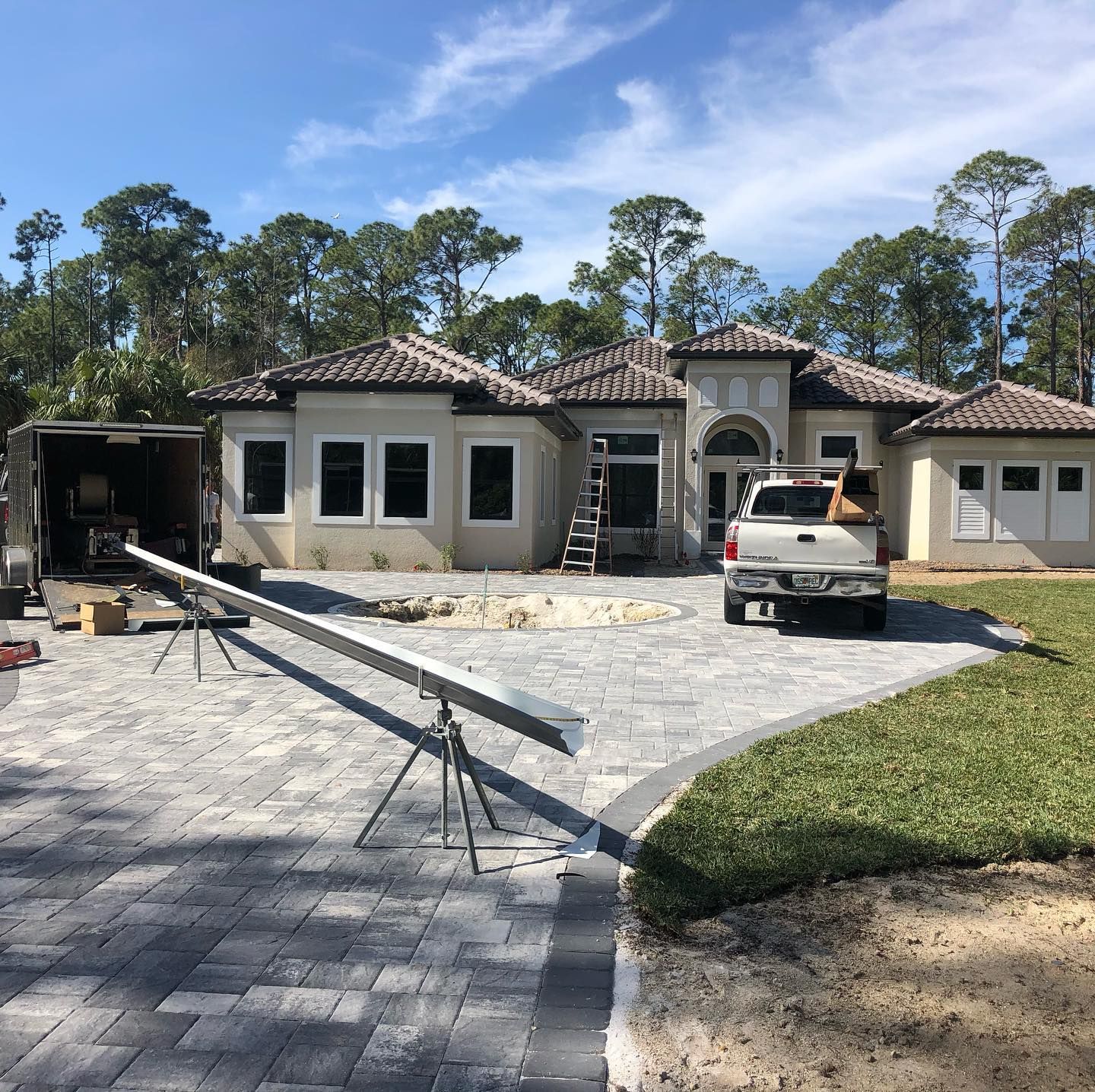 House construction site with truck, equipment, and new sod. Gray paver driveway.
