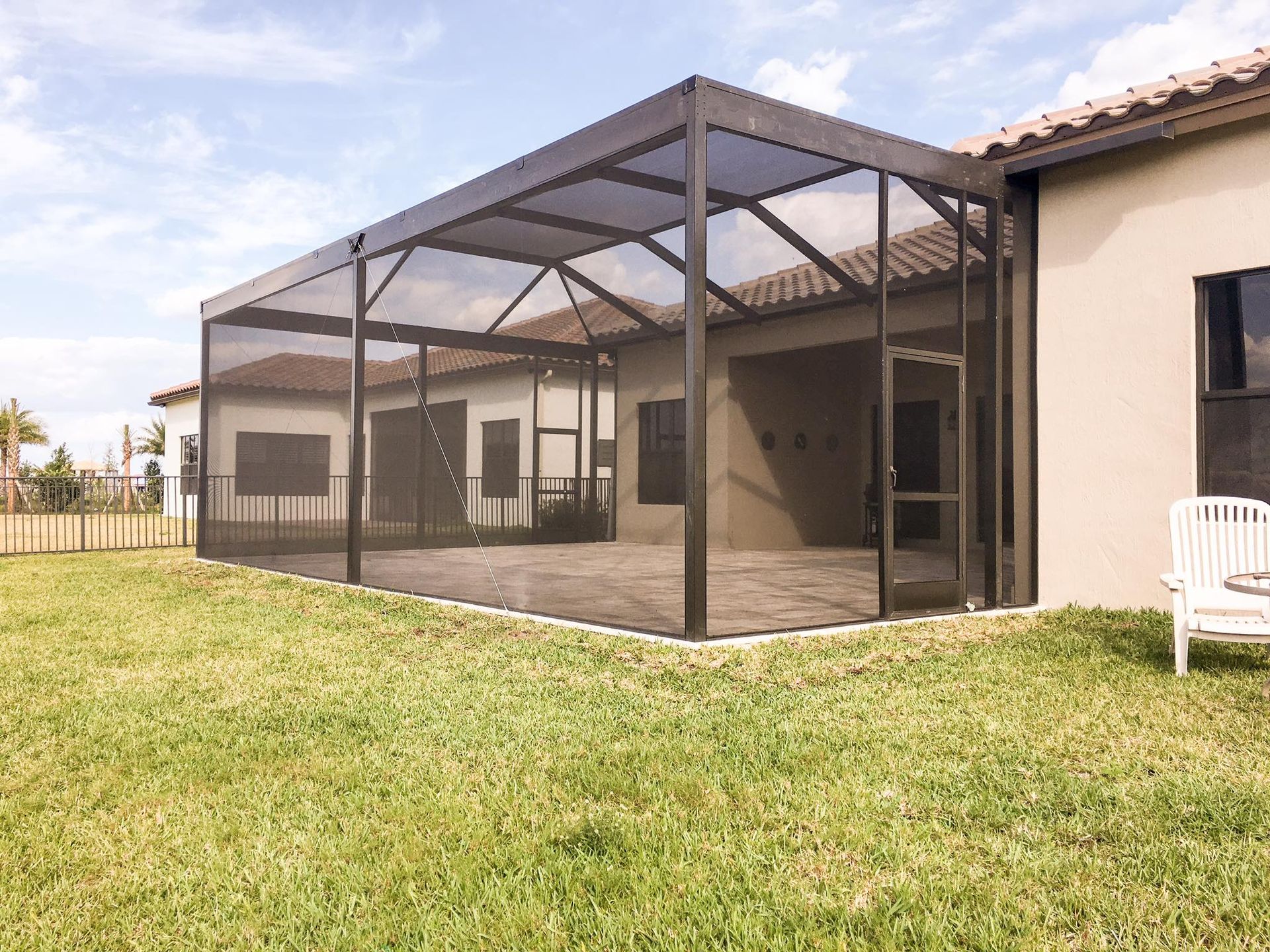 Screened-in patio extension attached to a light-colored house with dark framing, on a grassy lawn.