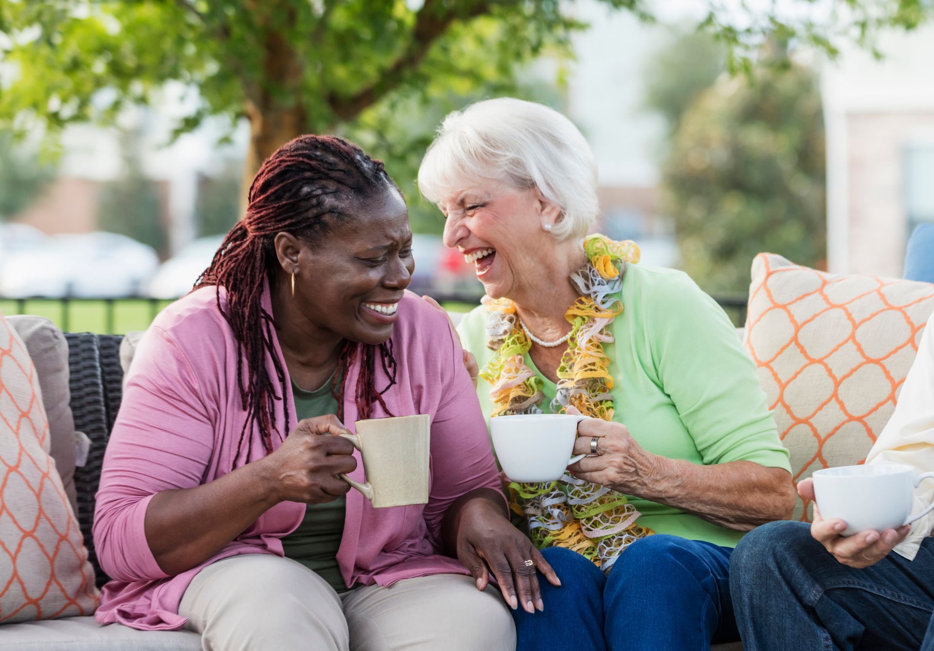 A group of older women are sitting on a couch drinking coffee and laughing.