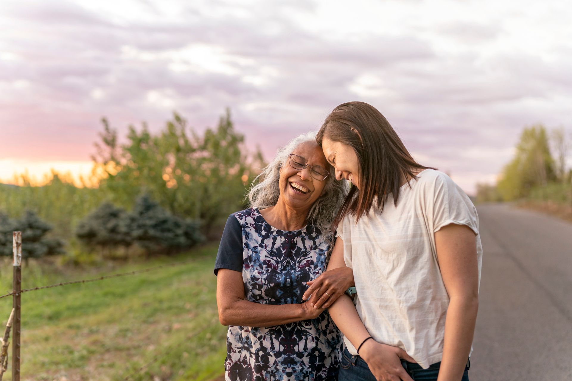 Two women are standing next to each other on the side of a road.