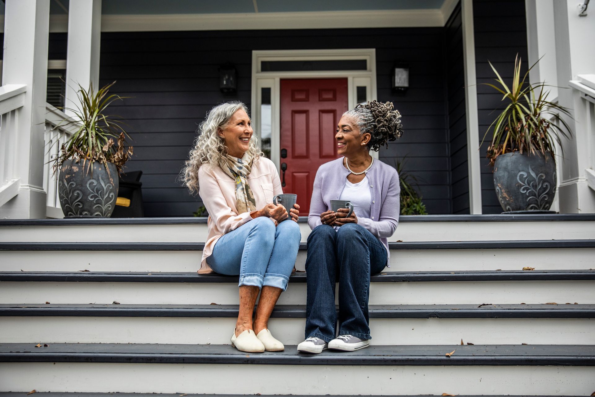Two women are sitting on the steps of a house drinking coffee.
