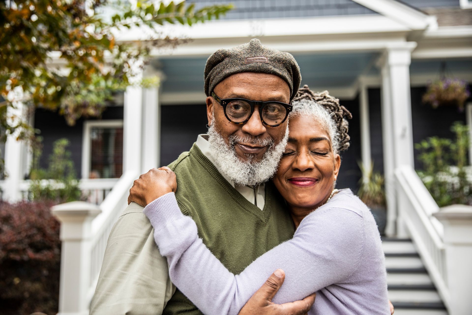 A man and a woman are hugging in front of a house.